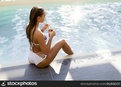 Beautiful slim young woman in bikini relaxing and drink cocktail on poolside of a swimming pool