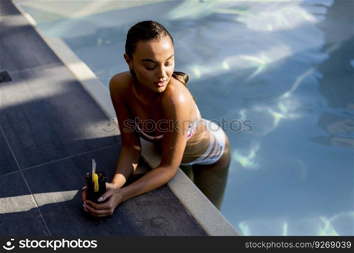 Beautiful slim young woman in bikini relaxing and drink cocktail on poolside of a swimming pool