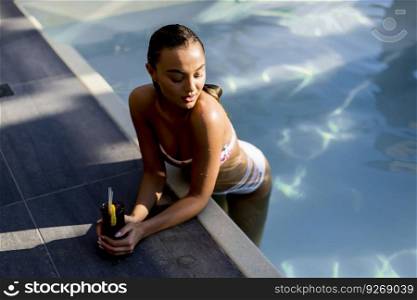 Beautiful slim young woman in bikini relaxing and drink cocktail on poolside of a swimming pool