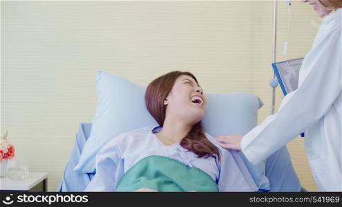 Beautiful smart Asian doctor and patient discussing and explaining something with clipboard in doctor hands while staying on Patient's bed at hospital. Medicine and health care concept.