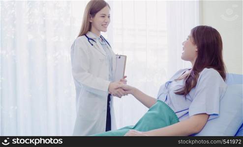 Beautiful smart Asian doctor and patient discussing and explaining something with clipboard in doctor hands while staying on Patient's bed at hospital. Medicine and health care concept.