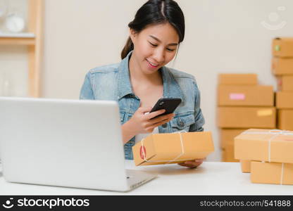 Beautiful smart Asian young entrepreneur business woman owner of SME checking product on stock scan qr code working at home. Small business owner at home office concept.