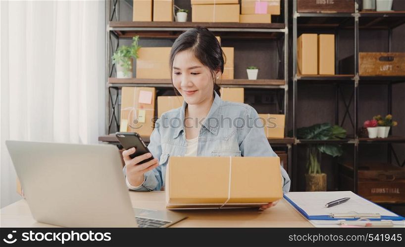 Beautiful smart Asian young entrepreneur business woman owner of SME checking product on stock scan qr code working at home. Small business owner at home office concept.