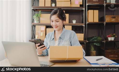 Beautiful smart Asian young entrepreneur business woman owner of SME checking product on stock scan qr code working at home. Small business owner at home office concept.
