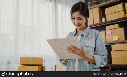 Beautiful smart Asian young entrepreneur business woman owner of SME checking product on stock and write on clipboard working at home. Small business owner at home office concept.