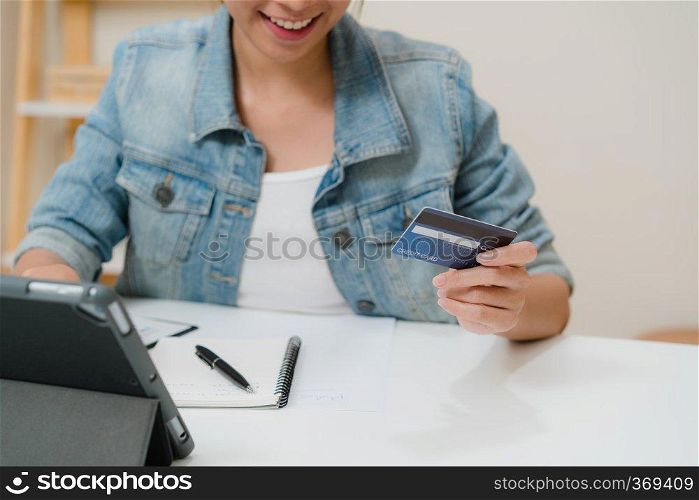 Beautiful smart business Asian woman using tablet buying online shopping by credit card while wear smart casual sitting on desk in living room at home. Lifestyle woman working at home concept.