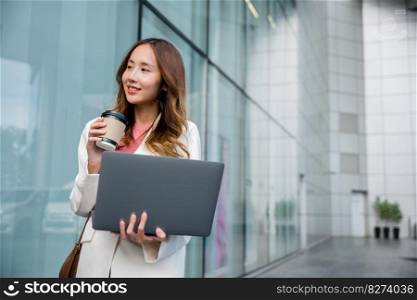 Beautiful smile female being ready to work. Business lifestyle concept. Confident businesswoman using computer laptop standing outdoor while drinking a cup of coffee takeaway at the city exterior