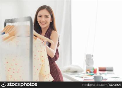 Beautiful Smiling Asian fashion designer stand and looking at camera in her workplace, looking at camera. Successful Young woman Relaxing with her small business. Entrepreneur, copy space.