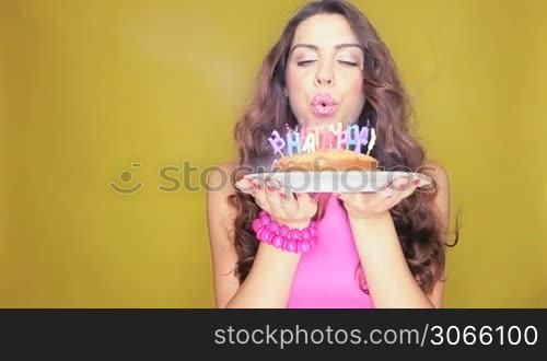 Beautiful smiling birthday girl holding her cake in both hands as she looks at all the burning candles