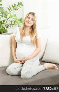 Beautiful smiling expectant mother sitting on sofa at living room