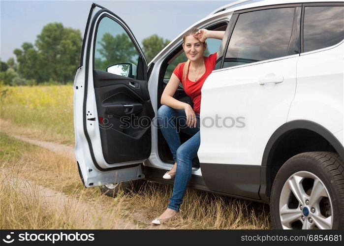 Beautiful smiling female driver relaxing in car at the field