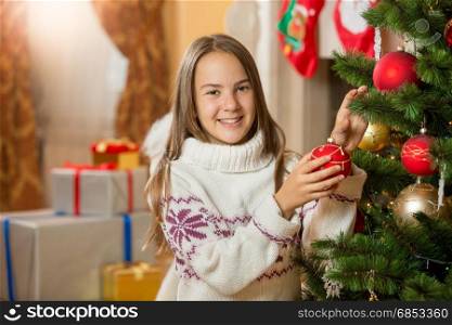 Beautiful smiling girl decorating Christmas tree with baubles