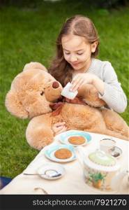 Beautiful smiling girl giving tea to plush bear