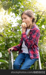 Beautiful smiling girl in checkered shirt posing in garden and biting apple