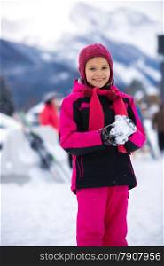 Beautiful smiling girl in pink ski suit making snowball