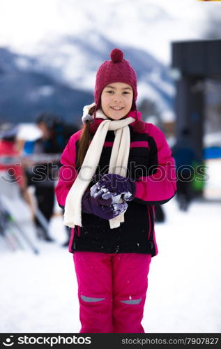 Beautiful smiling girl in pink ski suit posing against high mountain covered by snow