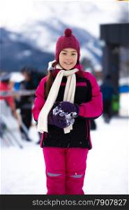 Beautiful smiling girl in pink ski suit posing against high mountain covered by snow
