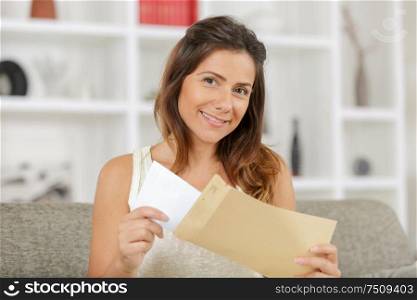 beautiful smiling girl sitting on sofa holding envelope