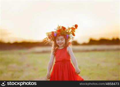 Beautiful smiling little girl in a red dress is spinning with a wreath on his head. Dancing in the field
