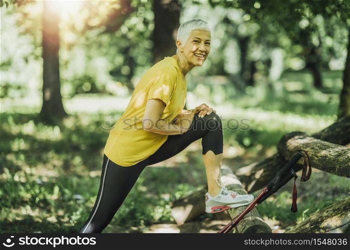 Beautiful smiling mature woman stretching legs after Nordic walking exercise. Stretching Legs after Nordic Walking Exercise