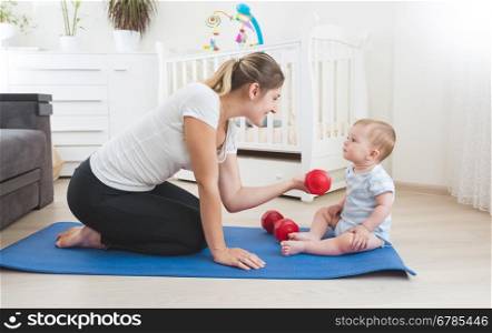 Beautiful smiling mother doing physical exercise with her baby on floor at living room