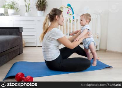 Beautiful smiling mother practicing yoga on fitness mat at living room