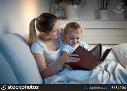 Beautiful smiling mother reading story to her baby boy before going to sleep