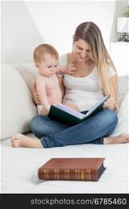 Beautiful smiling mother showing images in old book to her 9 months old baby boy