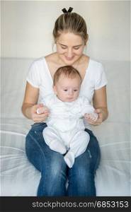 Beautiful smiling mother sitting on bed and holding her baby boy