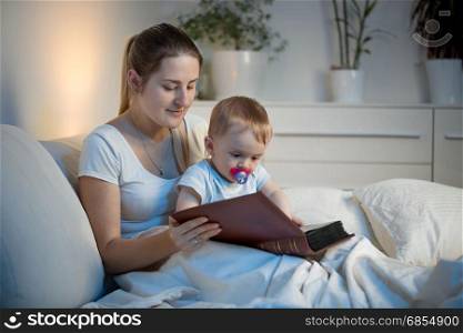 Beautiful smiling mother telling story to her baby at bed before going to sleep
