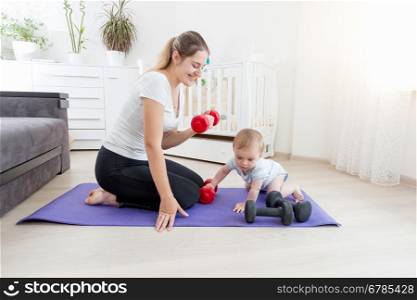 Beautiful smiling mother with her baby boy exercising on floor with dumbbells