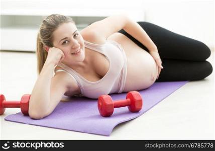 Beautiful smiling pregnant woman relaxing after exercising on fitness mat