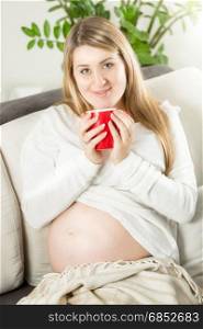 Beautiful smiling pregnant woman relaxing on sofa with cup of tea
