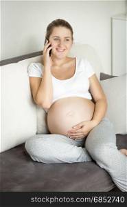 Beautiful smiling pregnant woman talking by phone on the sofa