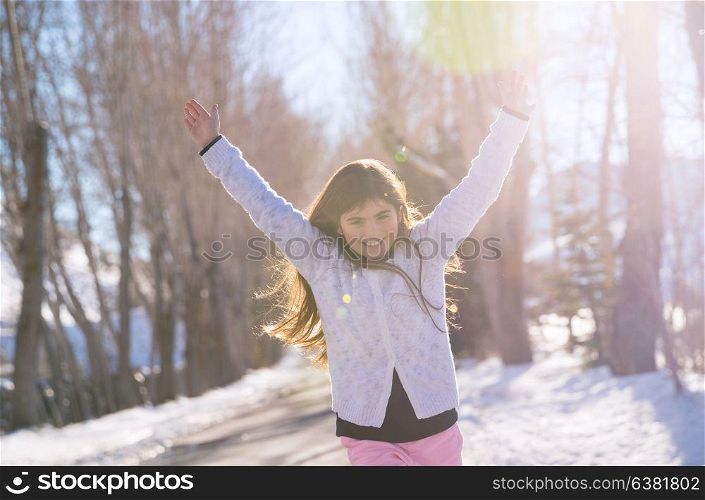 Beautiful smiling schoolgirl with raised up hands enjoying warm sunny weather in the wintertime in the park, happy winter holidays concept
