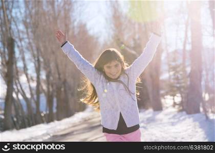 Beautiful smiling schoolgirl with raised up hands enjoying warm sunny weather in the wintertime in the park, happy winter holidays concept