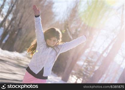 Beautiful smiling schoolgirl with raised up hands enjoying warm sunny weather in wintertime in the park, happy winter holidays, baby in good health embrasing life, wellness concept