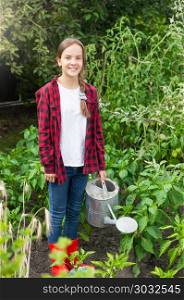 Beautiful smiling teenage girl in rubber boots with watering can working in garden. Smiling teenage girl in rubber boots with watering can working in garden