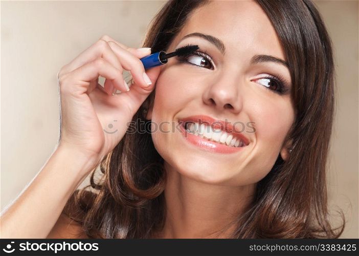 Beautiful smiling woman applying mascara on her eyelashes