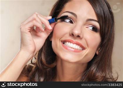 Beautiful smiling woman applying mascara on her eyelashes