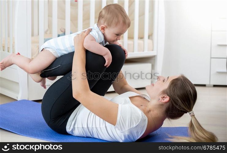 Beautiful smiling woman doing yoga exercise with her baby in living room