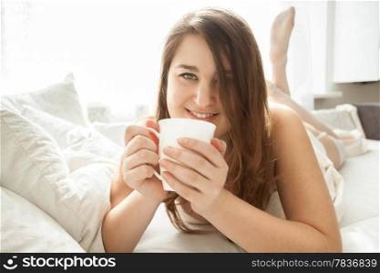 Beautiful smiling woman drinking coffee in bed at morning