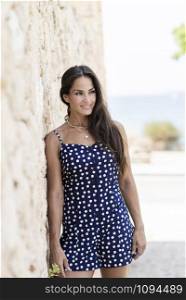 Beautiful smiling woman in blue dress leaning on wall while looking away