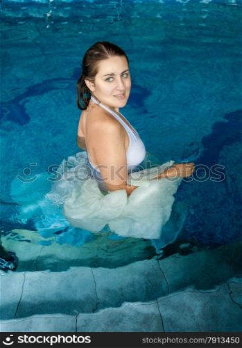 Beautiful smiling woman in white dress walking in swimming pool