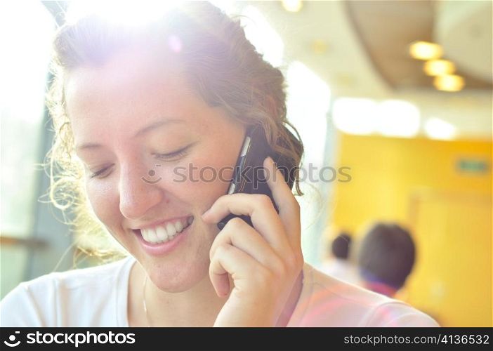 beautiful smiling woman is talking phone and looking downwards in sunny cafe