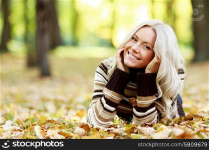 Beautiful smiling woman laying down on dry autumn leaves. Woman on autumn leaves