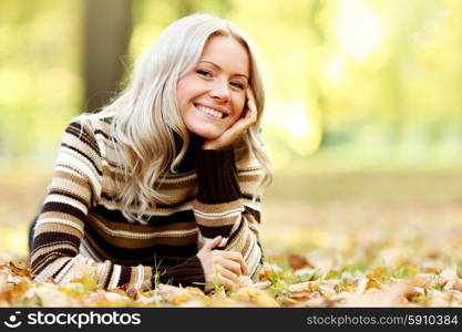 Beautiful smiling woman laying down on dry autumn leaves. Woman on autumn leaves