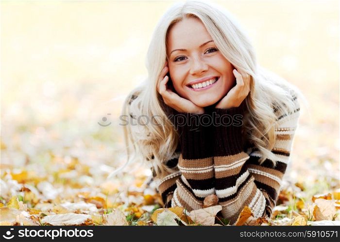 Beautiful smiling woman laying down on dry autumn leaves. Woman on autumn leaves