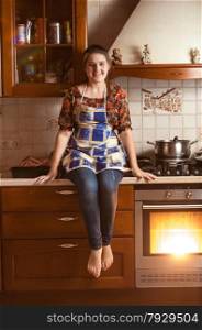 Beautiful smiling woman sitting on tabletop while baking in oven