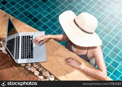 Beautiful smiling woman using laptop computer in swimming pool, blue water